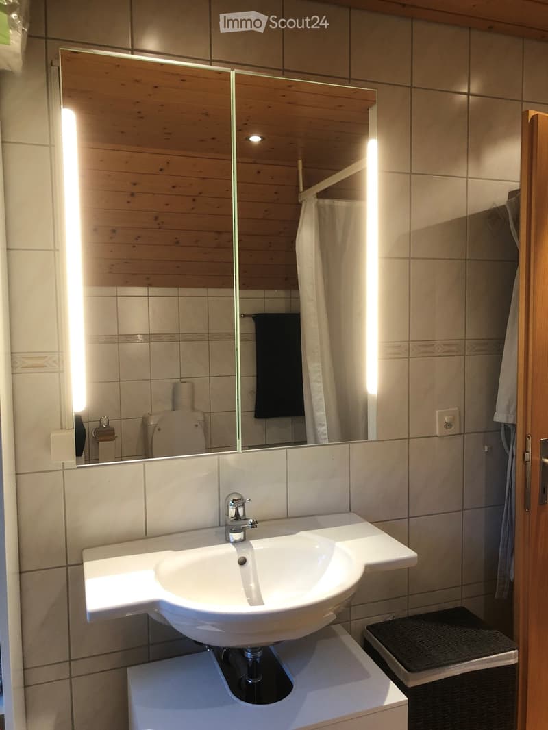 Modern bathroom with a white sink, chrome faucet, large mirror, toilet, and a black towel hanging on the side.