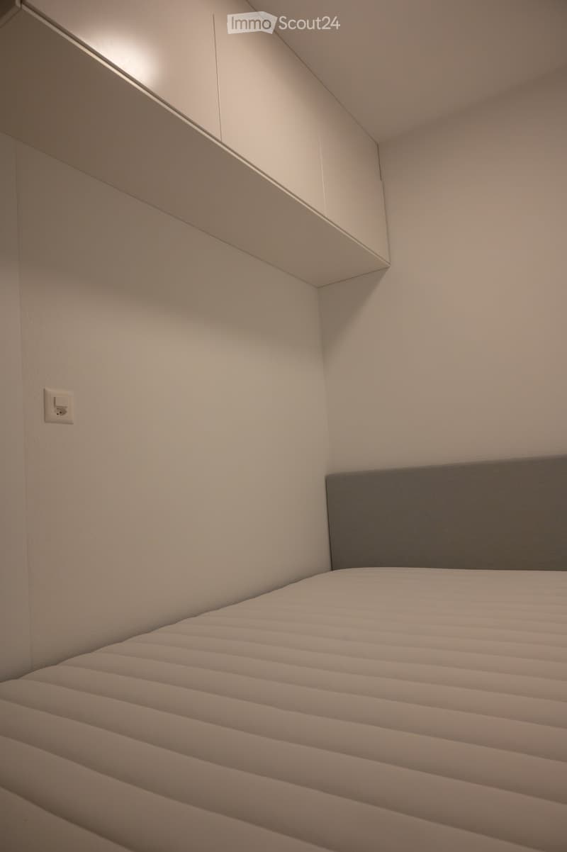 Modern bedroom with a white bed and grey headboard, featuring sleek design and minimalistic decor.