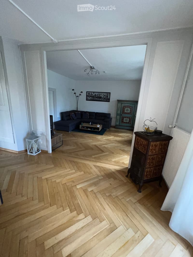 Living room with herringbone wooden flooring, dark grey sectional sofa, coffee table, side table, picture frame, floor lamp, and a decorative cabinet.