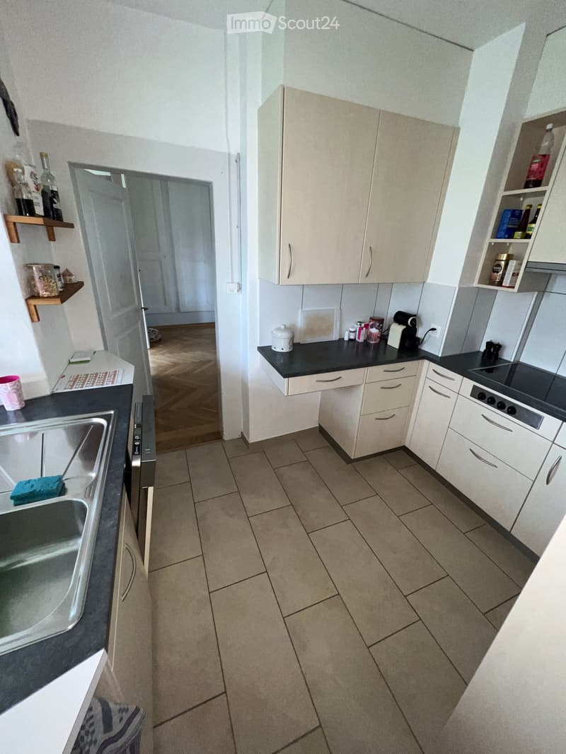 Modern kitchen with white cabinets, black countertops, and tiled floor. Includes a sink, fridge, oven, and various small appliances.