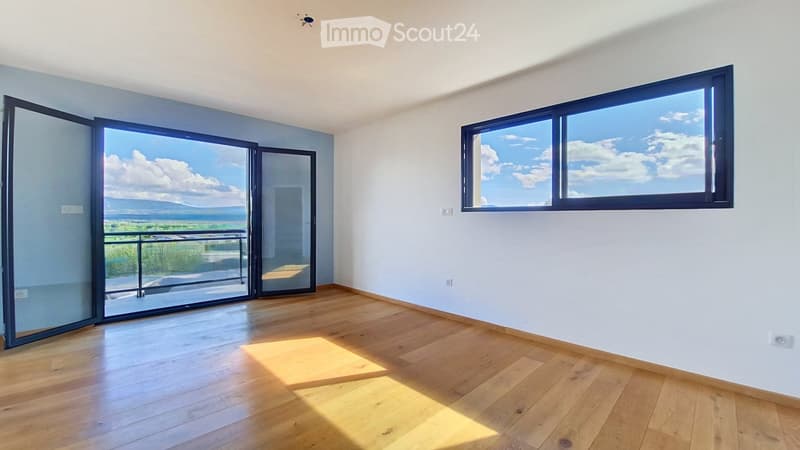 Empty room with wooden flooring, large windows, and sliding glass doors leading to a balcony with a scenic view.