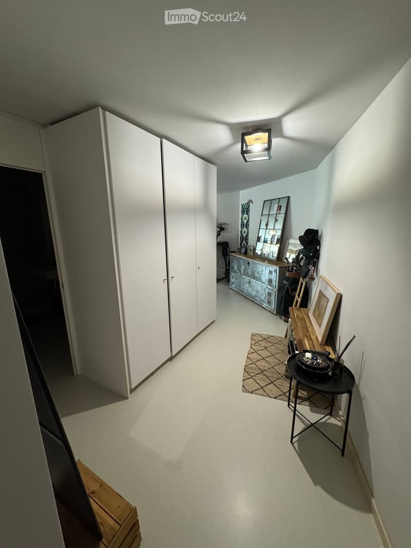 Hallway with white walls, light-colored flooring, and a small table with a mirror and decorative items.