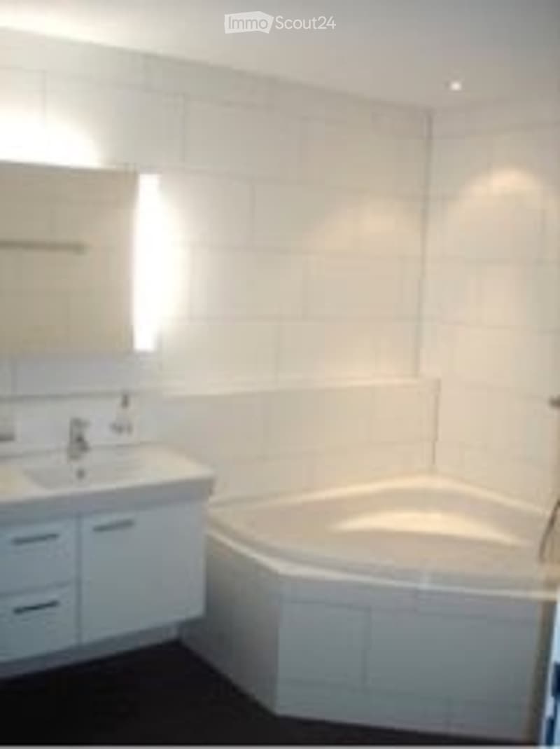 Modern bathroom with a large, corner bathtub, a white sink with a mirror, and white cabinets.