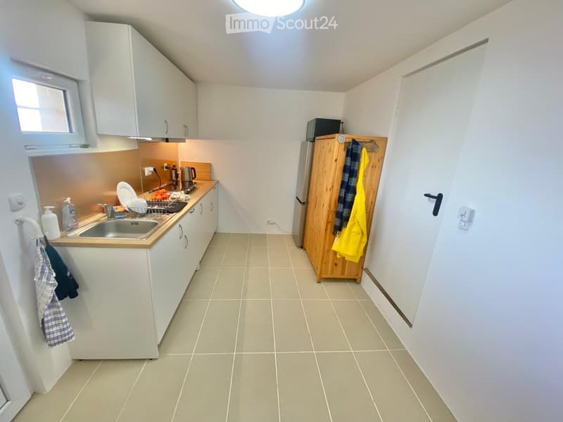 Modern kitchen with white cabinets, a stainless steel sink, a wooden cabinet, and a refrigerator. The countertop has a dish rack, a kettle, and various kitchen items.