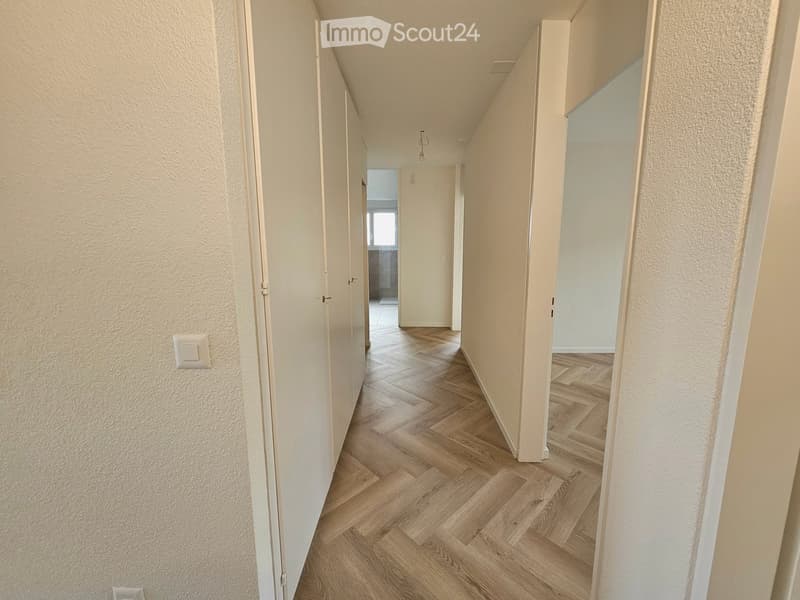 A narrow hallway with wooden flooring, white walls, and several closed doors leading to other rooms.