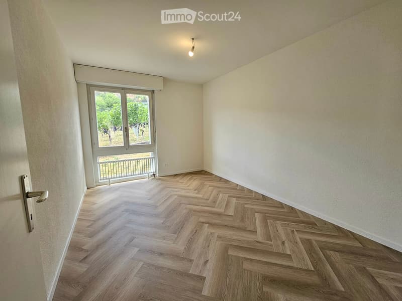 Empty room with herringbone wooden flooring, white walls, and a large window with a metal railing leading to an outdoor area.