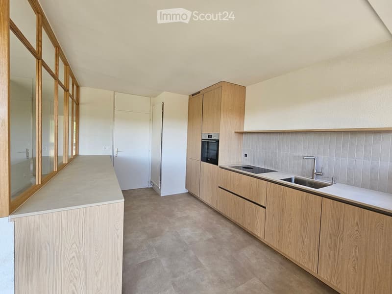 Modern kitchen with light wooden cabinets, a central island, and built-in appliances including a sink, faucet, and oven.
