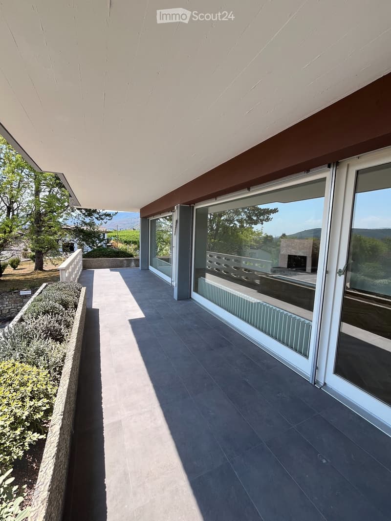 Modern balcony with large glass sliding doors, tiled floor, and a view of greenery and mountains.