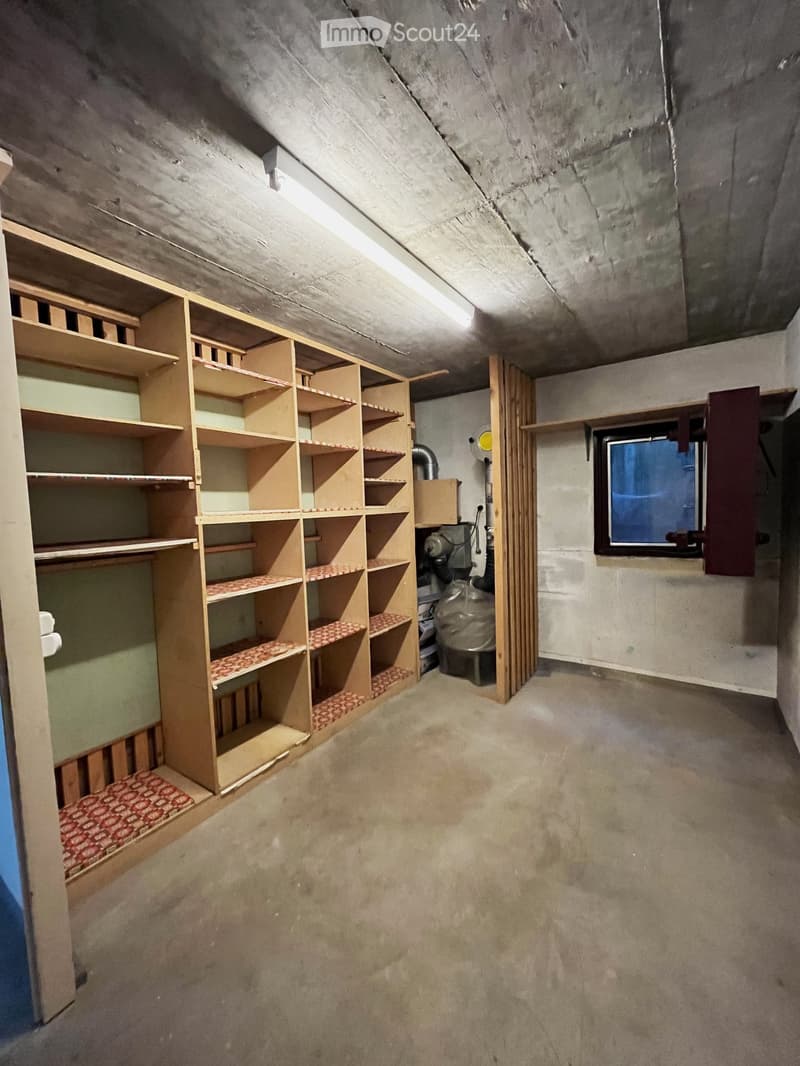 Empty attic space with exposed wooden beams, built-in wooden shelving units, and a small window. The floor is unfinished concrete.