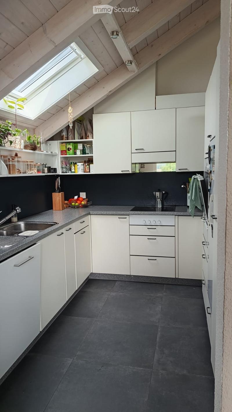 Modern kitchen with white cabinets, dark countertops, and a black tiled floor. Features include a sink, faucet, knife block, coffee maker, and a window with a skylight above.