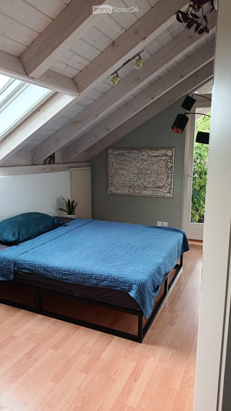 Cozy attic bedroom with wooden slanted ceilings, skylights, a double bed with blue bedding, a potted plant, and a decorative wall art piece.