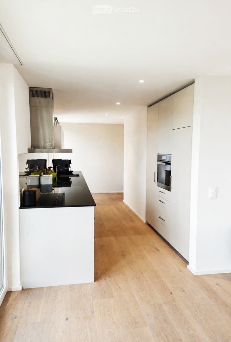 Modern kitchen with white cabinets, light wooden flooring, and stainless steel appliances including an oven and coffee maker.