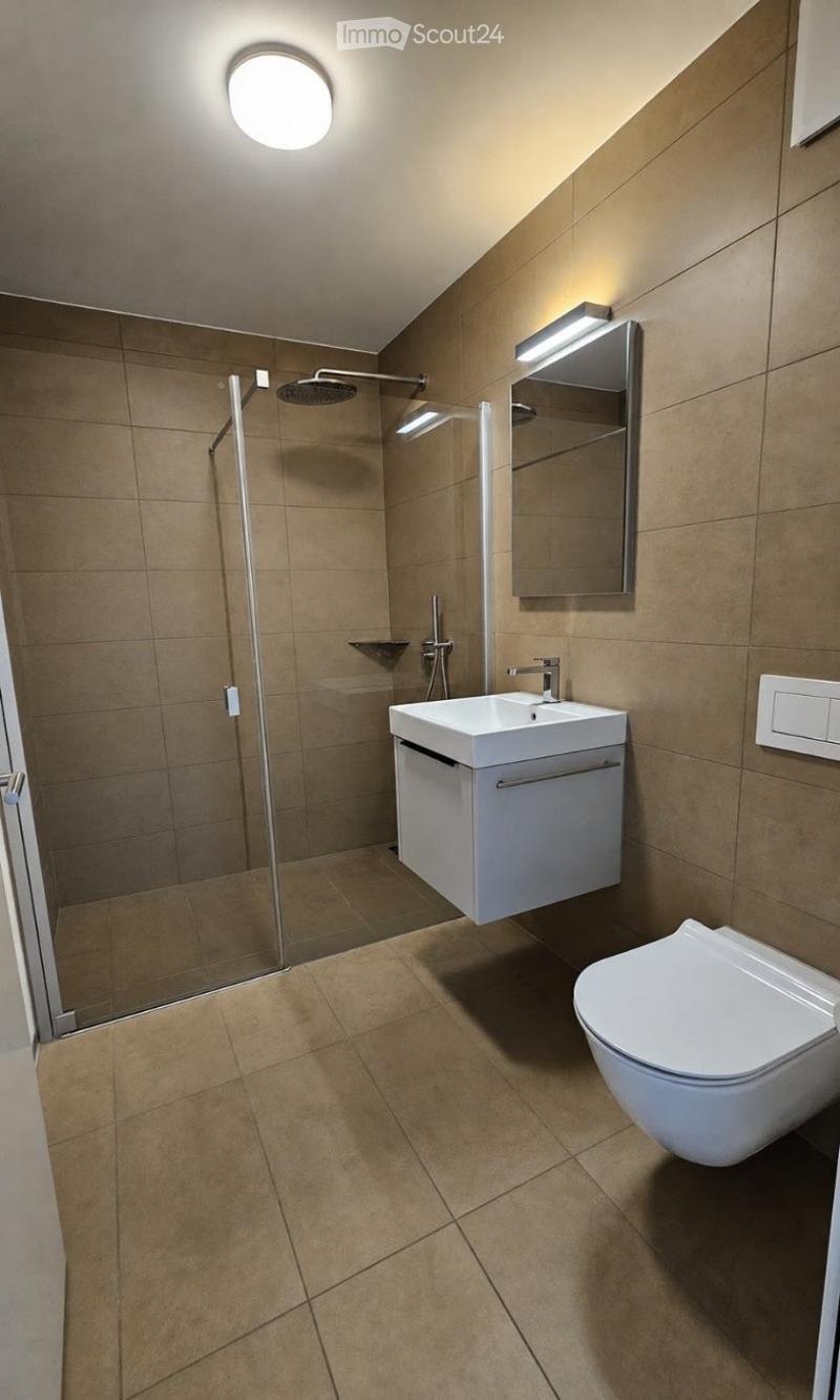 Modern bathroom with beige tiles, a glass-enclosed shower, a white sink with a cabinet, and a toilet.
