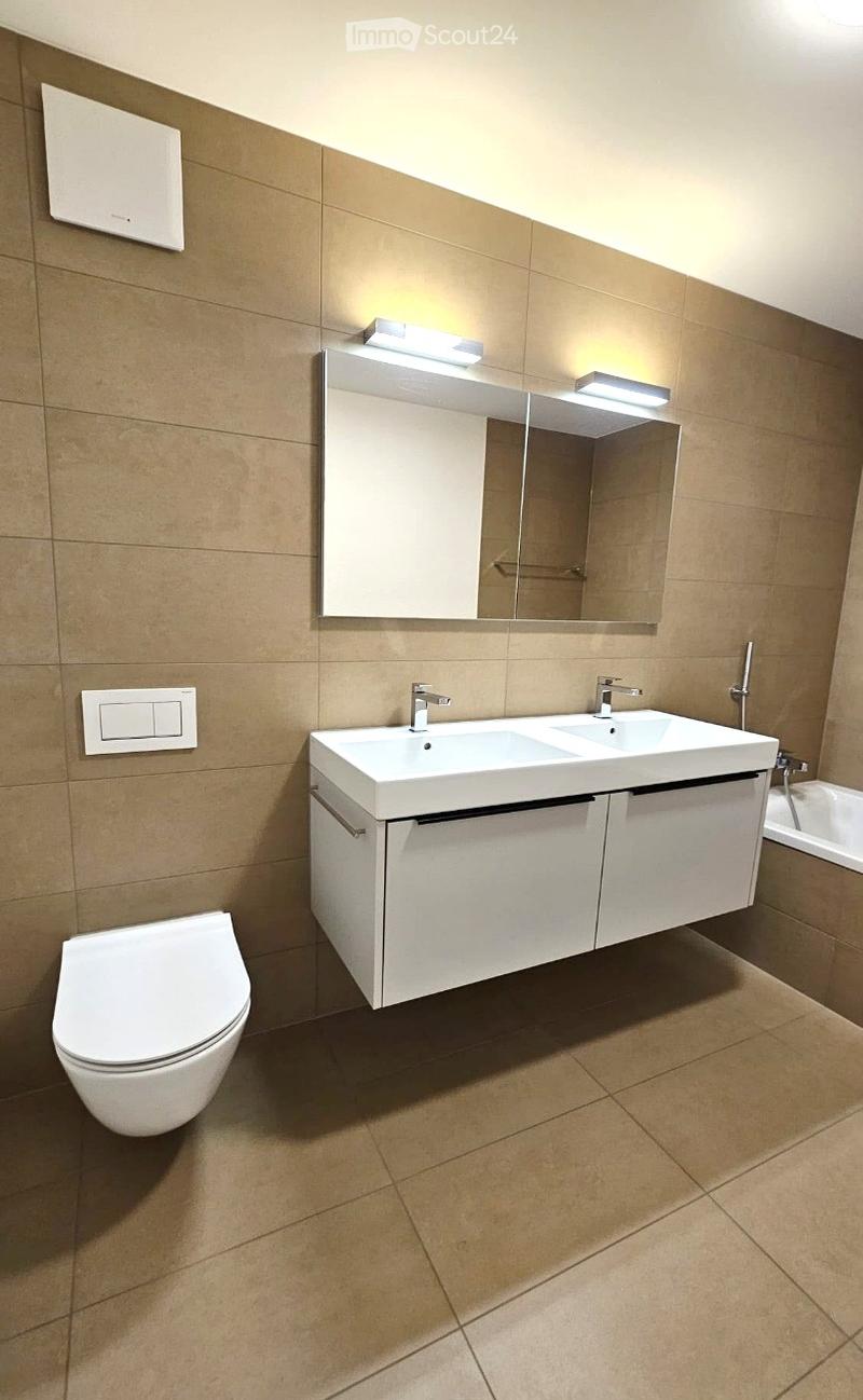 Modern bathroom with beige tiles, a white toilet, a double sink with a mirrored cabinet, and built-in storage cabinets.