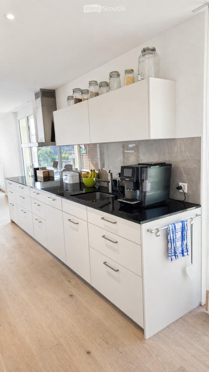 Modern kitchen with white cabinets, black countertop, stainless steel sink, coffee maker, and various jars on the countertop.