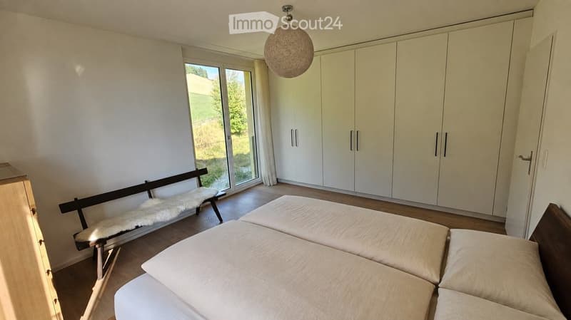 Bright bedroom with white walls, large window, white wardrobe, sofa, bench with fur throw, and a hanging spherical lamp.