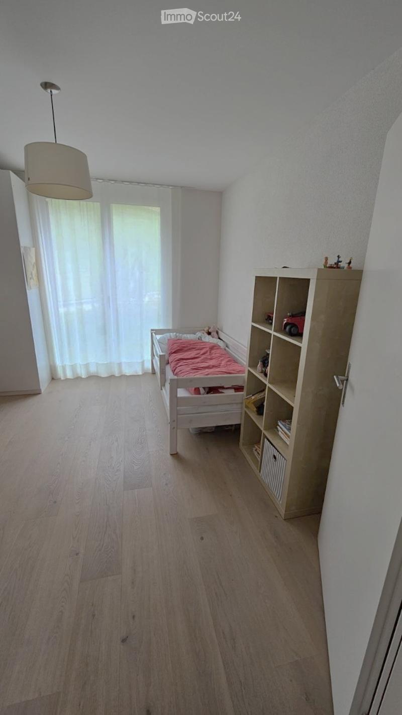 Cozy bedroom with wooden flooring, a single bed with a red blanket, a bookshelf, and a hanging lamp.