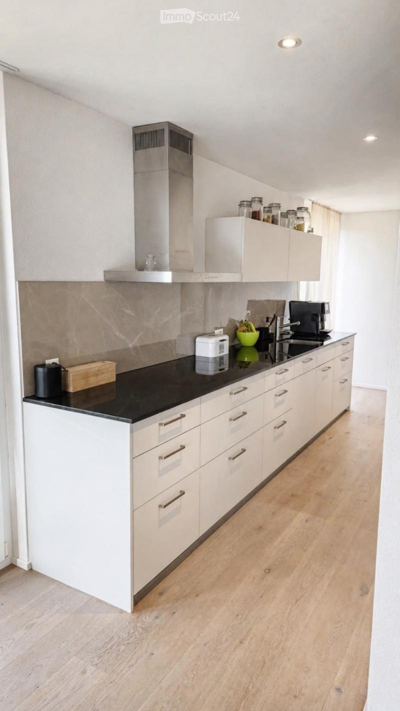 Modern kitchen with white cabinets, black countertop, stainless steel appliances, and wooden flooring.