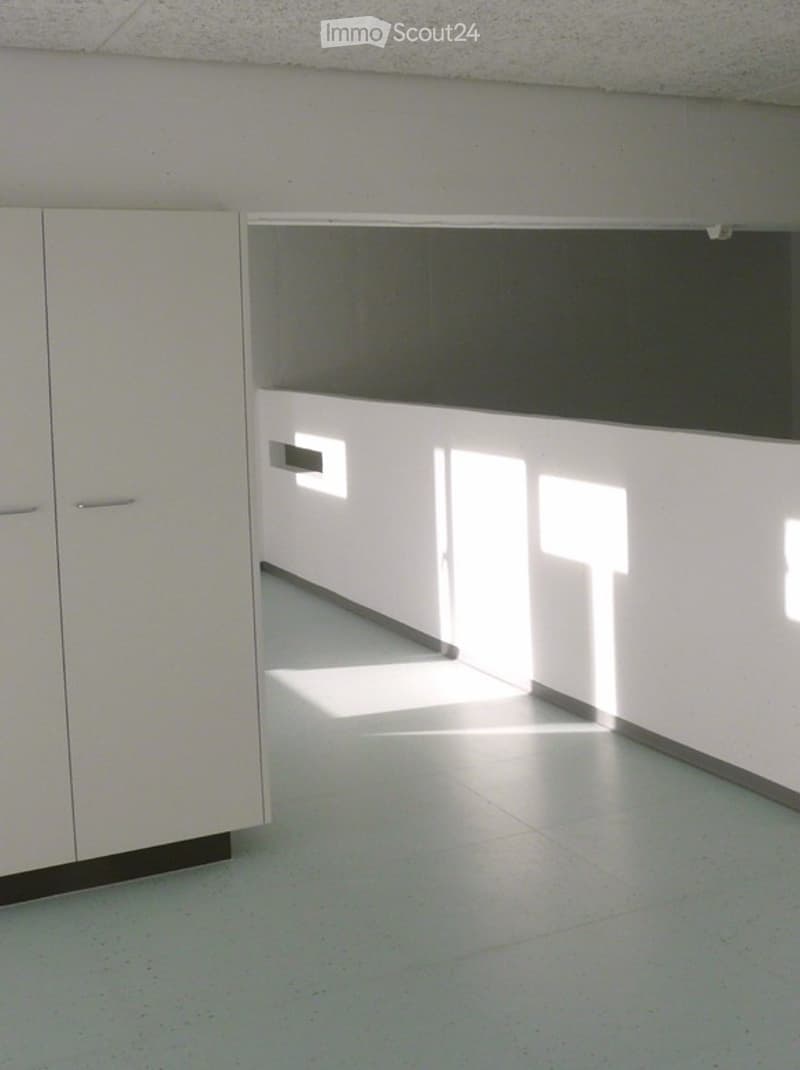 Empty kitchen area with white cabinets and a tiled floor, illuminated by natural light from a window.