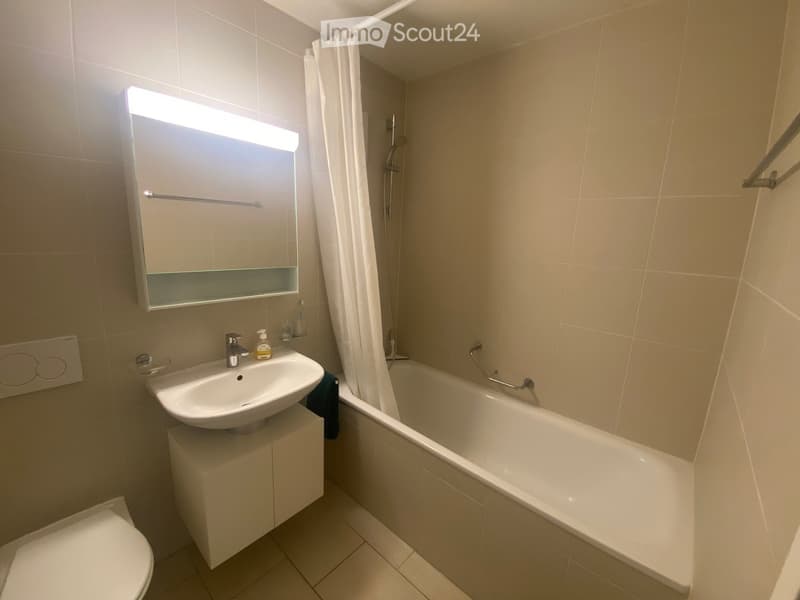 Modern bathroom with a white sink, bathtub, toilet, and a mirrored cabinet with built-in lighting. The space features beige tiles and a sleek design.