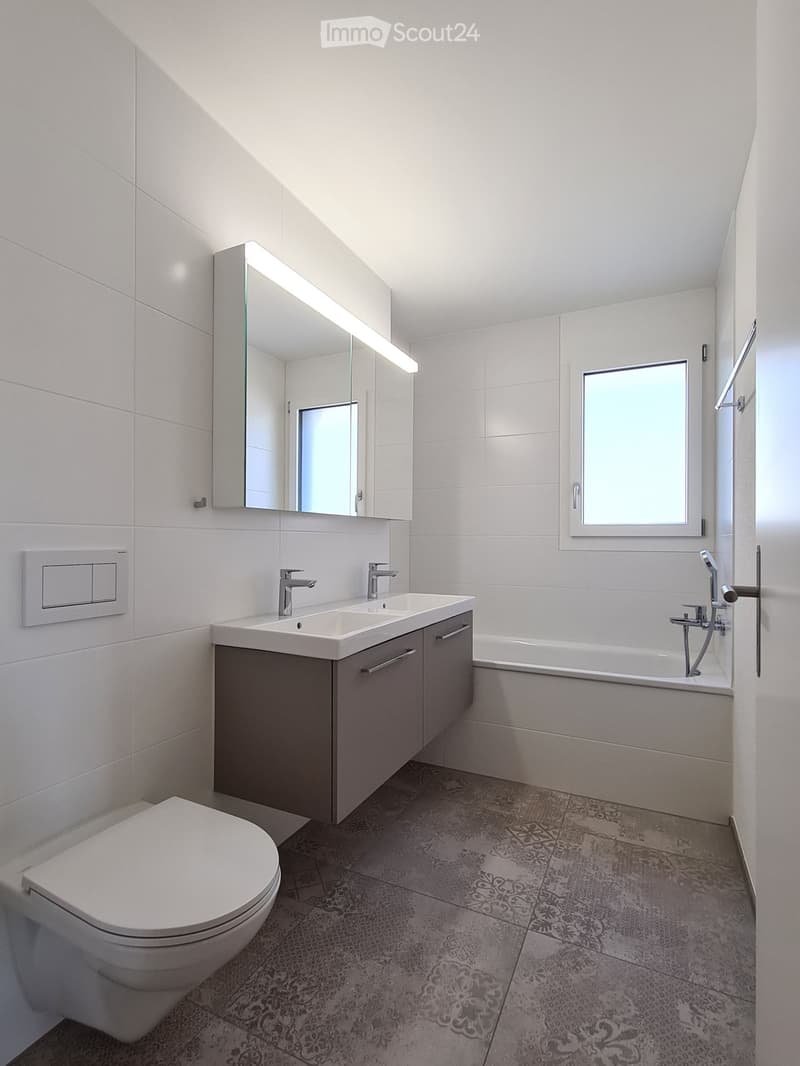modern bathroom with white tiles, mirror, double sink, bathtub, and toilet
