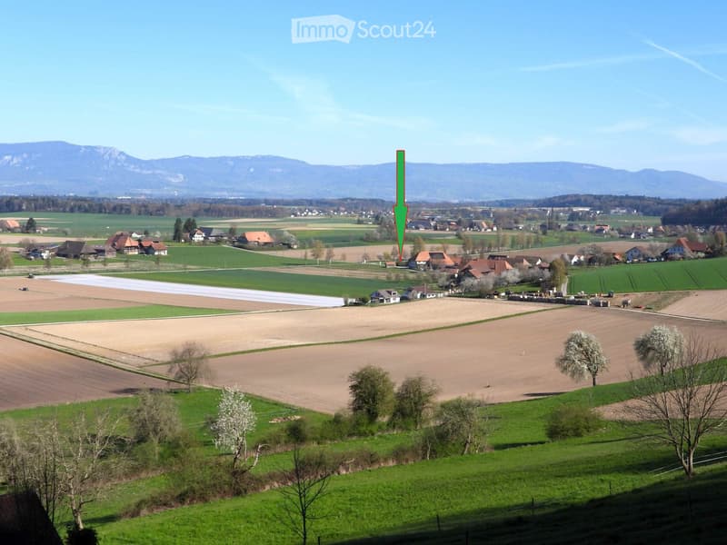 Aerial view of a rural landscape with fields, houses, and mountains in the background.