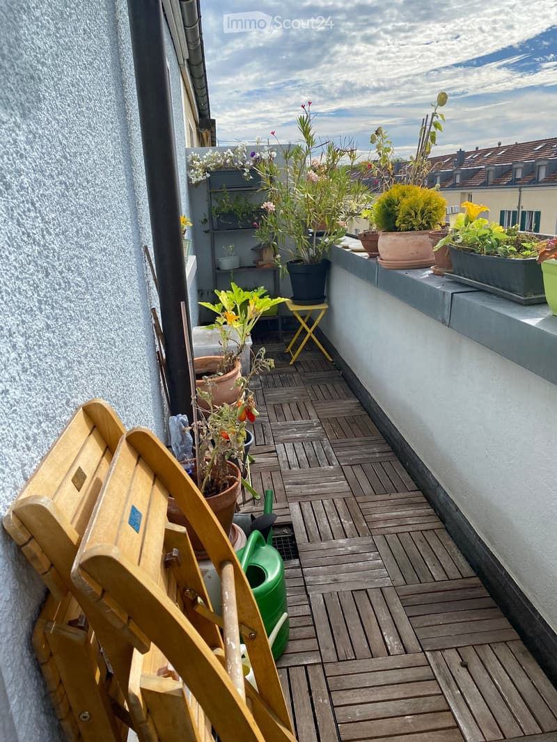 Wooden decked balcony with potted plants, a yellow folding chair, and a green watering can.