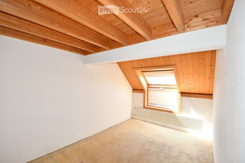Empty room with white walls, wooden ceiling, and tiled floor. Features a skylight window and a radiator under the window.