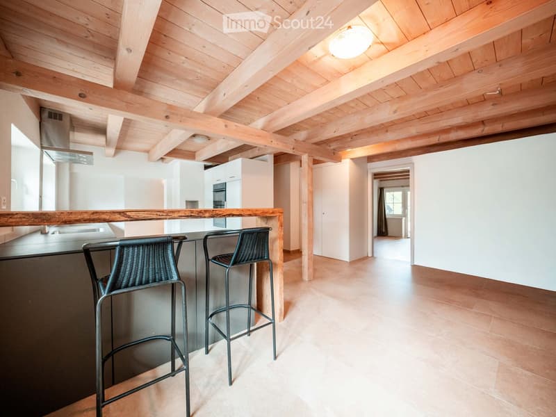 Modern kitchen with exposed wooden beams, white cabinets, stainless steel appliances, and a wooden island with bar stools.