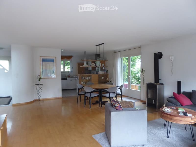 Open-plan living and dining area with wooden flooring, a grey sofa, coffee table, dining table with chairs, and a modern fireplace.