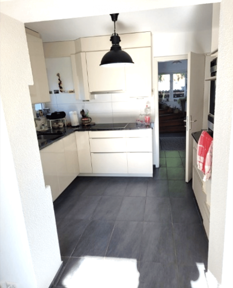 Modern kitchen with white cabinets, dark tiled floor, and stainless steel appliances including a sink, fridge, oven, and microwave. A coffee maker and other small items are on the counter.
