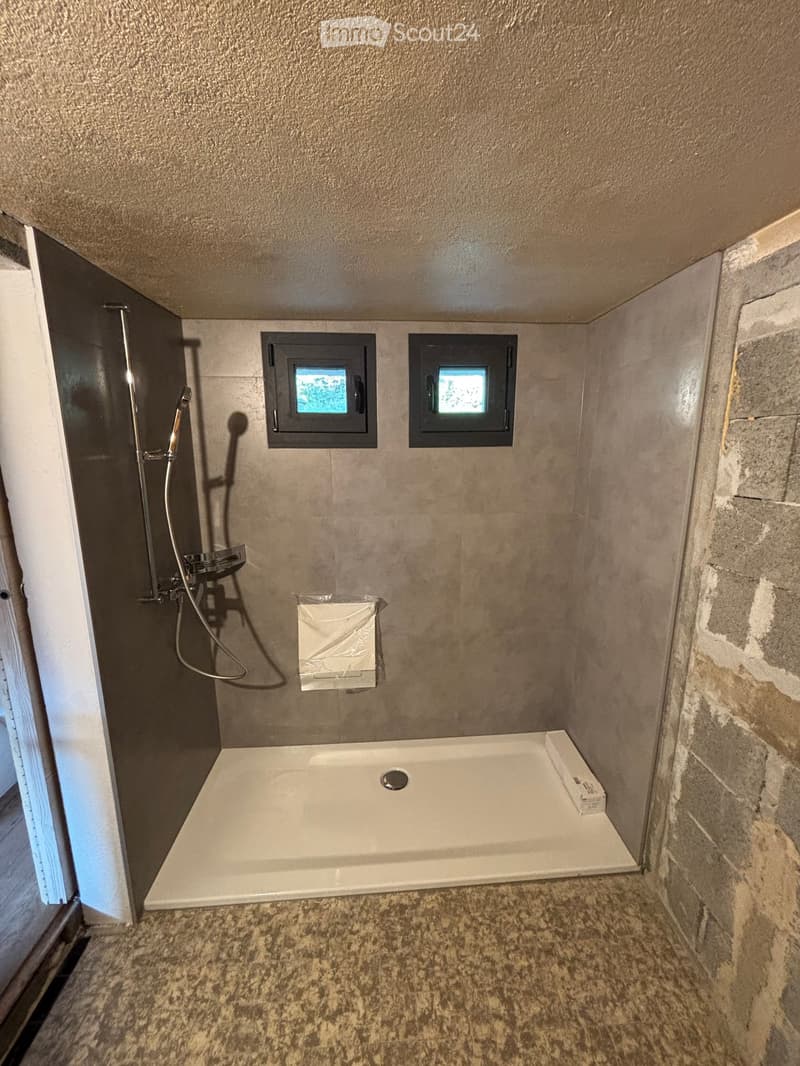 Modern bathroom with a shower stall, granite flooring, and two windows offering a view.