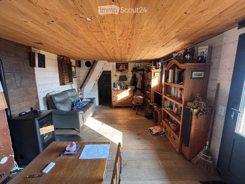 Cozy living room with wooden beams, exposed wooden floor, and a mix of modern and rustic furniture including a sofa, table, bookshelf, and fireplace.