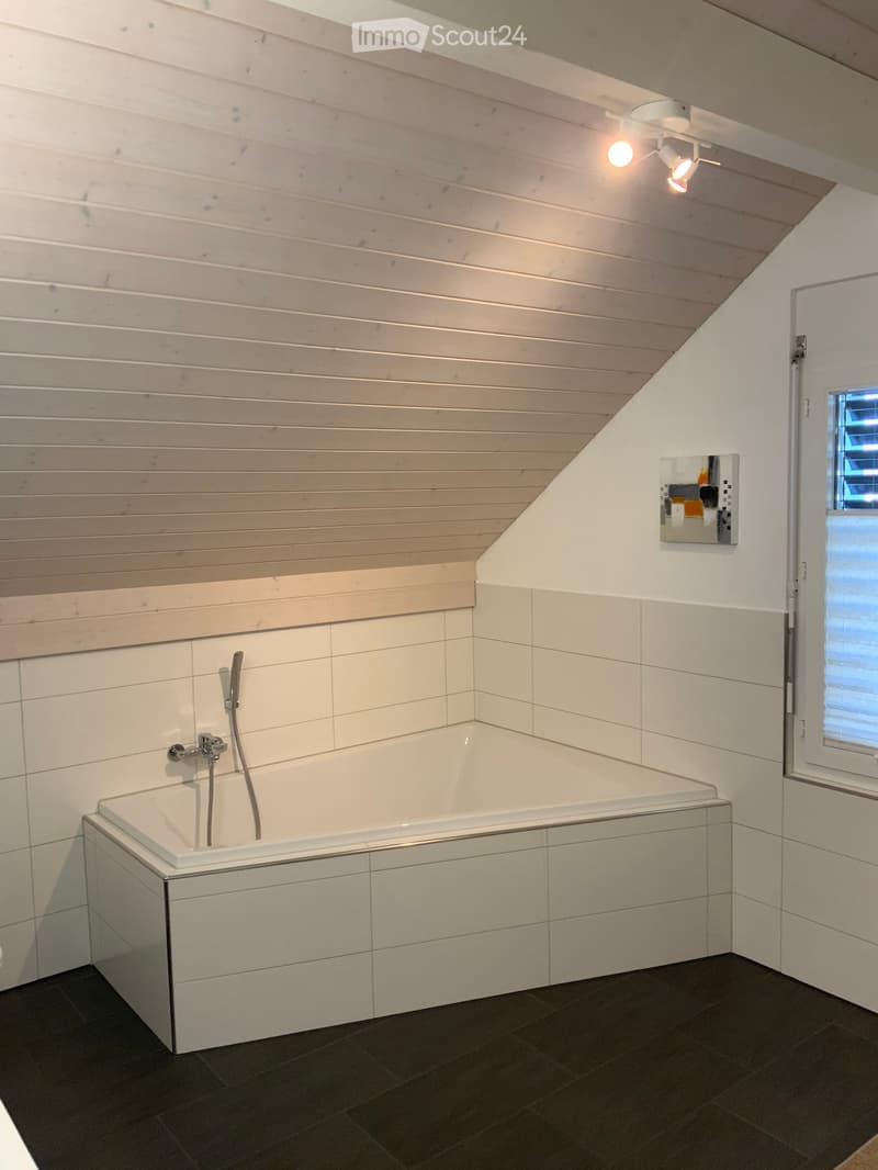 white bathtub, white tiled walls, wooden ceiling, spotlights, open door, picture on wall