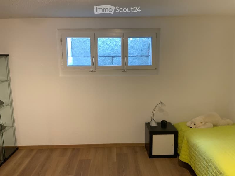 A room with a yellow bed, white walls, wooden floor, a lamp on a nightstand, and a glass cabinet.