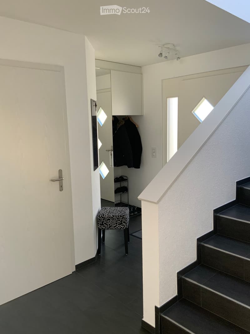 Entrance hall with tile flooring, white doors, stairs, bench, clothing on hangers, closet, mirror with geometric patterns, small shelf, door switch.