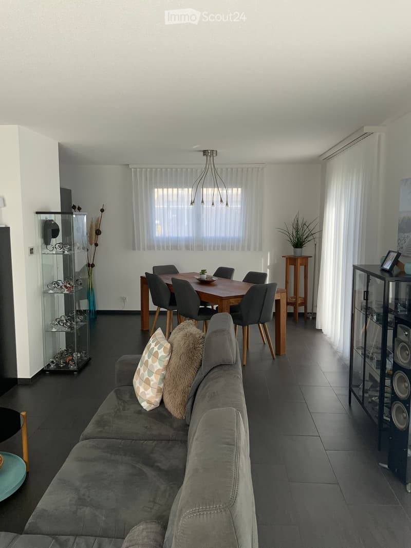 Modern living room with gray couch, wooden table, white wall, window, chandelier, potted plant