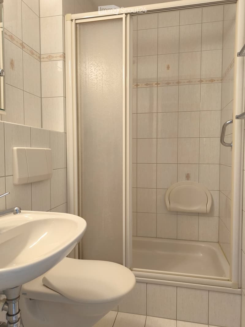 Bathroom with white tiles, shower, toilet, sink, and faucet