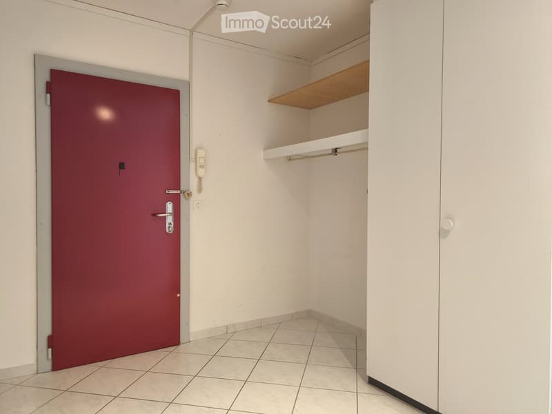 Empty room with white tiles, red door, white walls, white wardrobe, shelf, and telephone
