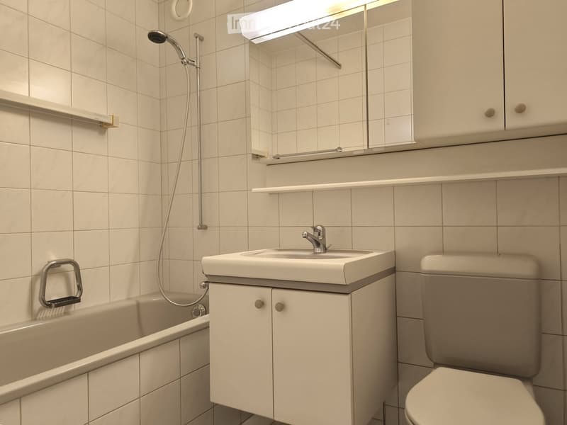 Bathroom with bathtub, sink, toilet, shower, white tiles, mirror, cabinet, and shower head.