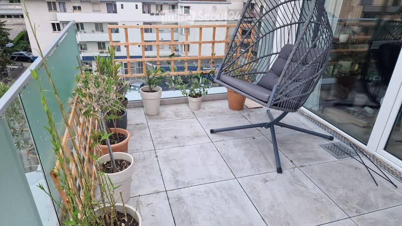 Balcony with a hanging egg chair, potted plants, and a wooden railing, overlooking a cityscape.