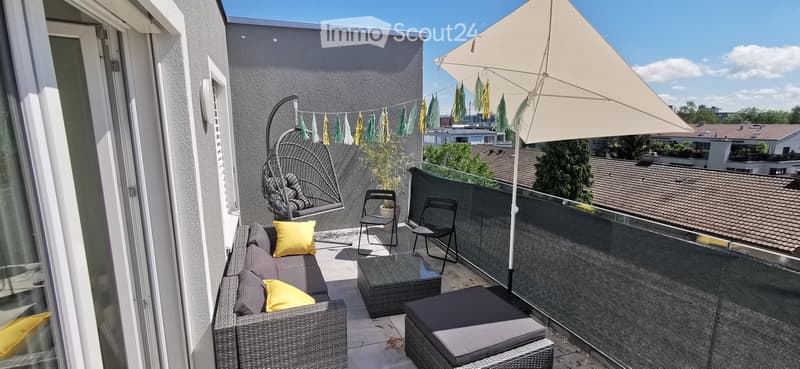 Balcony with wicker sofa, coffee table, chairs, hanging egg chair, umbrella, and decorative flags.