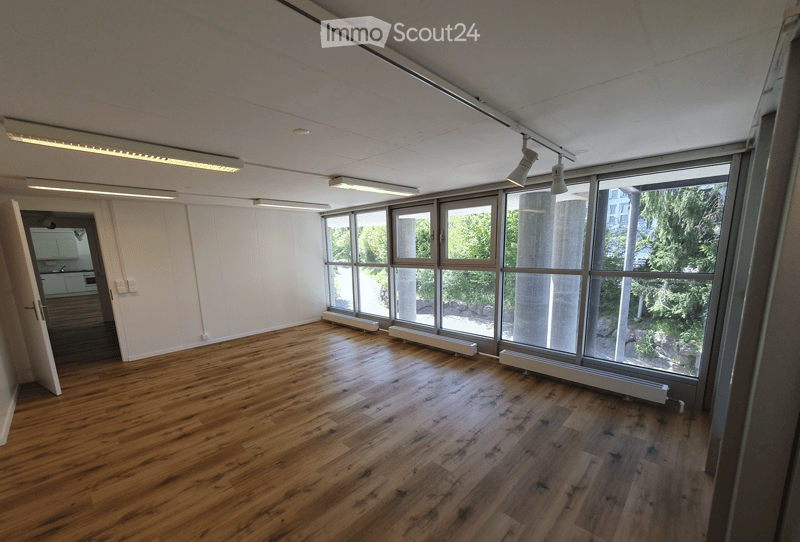 Empty room with wooden flooring, large windows, and exposed beams. No furniture or equipment present.