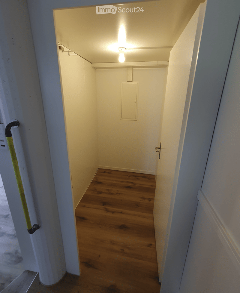 Empty hallway with wooden flooring, white walls, and a single light fixture on the ceiling. A broom is visible on the left side.