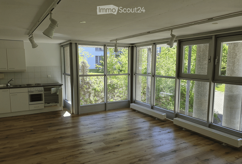 Open-plan space with wooden flooring, large windows, and built-in kitchen units including a sink, stove, and oven. The room is completely empty with no furniture or personal items.