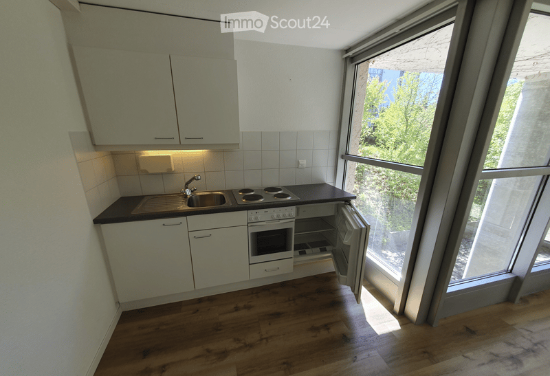 Modern kitchen with white cabinets, a sink, a stove, and an oven. The space features wooden flooring and large windows offering a view of greenery outside.
