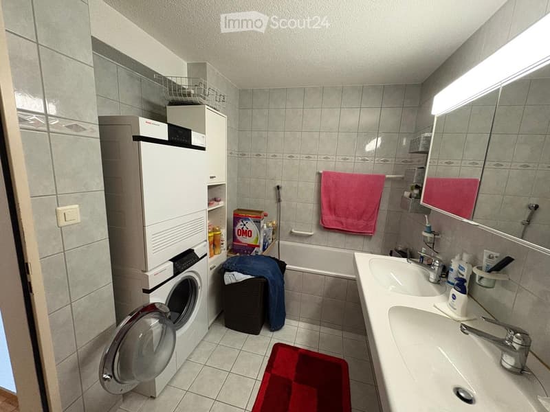 Bathroom with a double sink, mirror, washing machine, bathtub, and various toiletries.