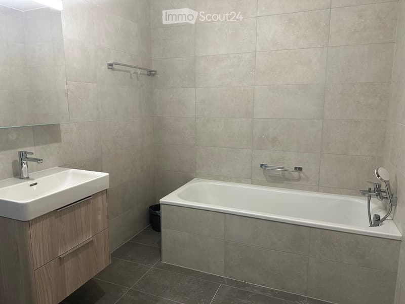 Modern bathroom with a white sink, wooden cabinet, bathtub, and modern fixtures.
