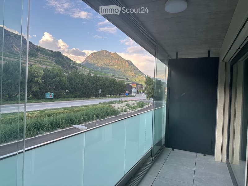 Modern balcony with glass railings, tiled floor, and scenic mountain view.