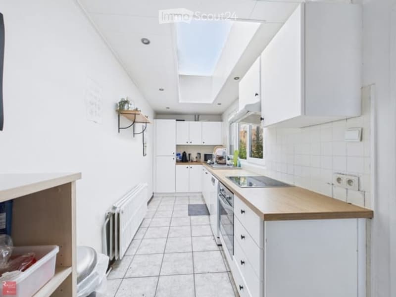 Bright, modern kitchen with white cabinets, a wooden countertop, and a skylight above. Includes a sink, oven, and a small shelf with a plant.